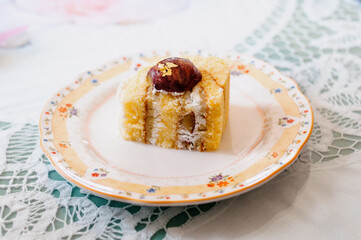 slice of layered chestnut cake with whipped cream on floral print ceramic plate on white lace table mat