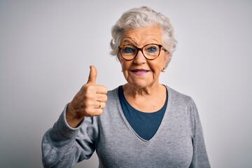 Senior beautiful grey-haired woman wearing casual sweater and glasses over white background doing happy thumbs up gesture with hand. Approving expression looking at the camera showing success.