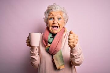 Senior beautiful grey-haired woman drinking mug of coffee over isolated pink background screaming...