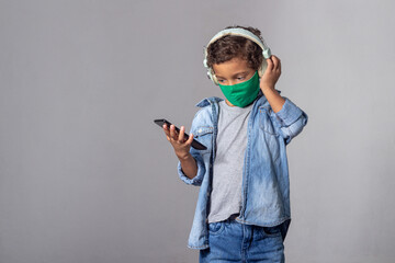 White boy with curly hair wearing protection mask against covid-19 with smartphone listening to music with headphone