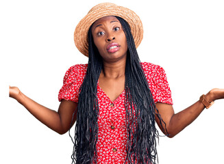 Young african american woman wearing summer hat clueless and confused expression with arms and...