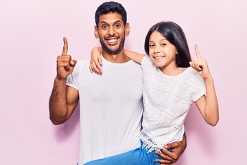 Latin father and daughter wearing casual clothes smiling with an idea or question pointing finger...