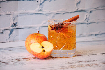 A whole and half-chopped ripe apple stand on a table near a crystal glass of siber with cinnamon...