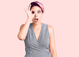 Fototapeta premium Young beautiful woman with pink hair wearing casual clothes doing ok gesture shocked with surprised face, eye looking through fingers. unbelieving expression.