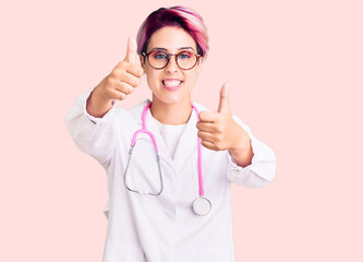 Young beautiful woman with pink hair wearing doctor uniform approving doing positive gesture with hand, thumbs up smiling and happy for success. winner gesture.