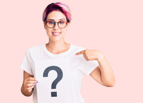 Young beautiful woman with pink hair holding question mark pointing finger to one self smiling happy and proud