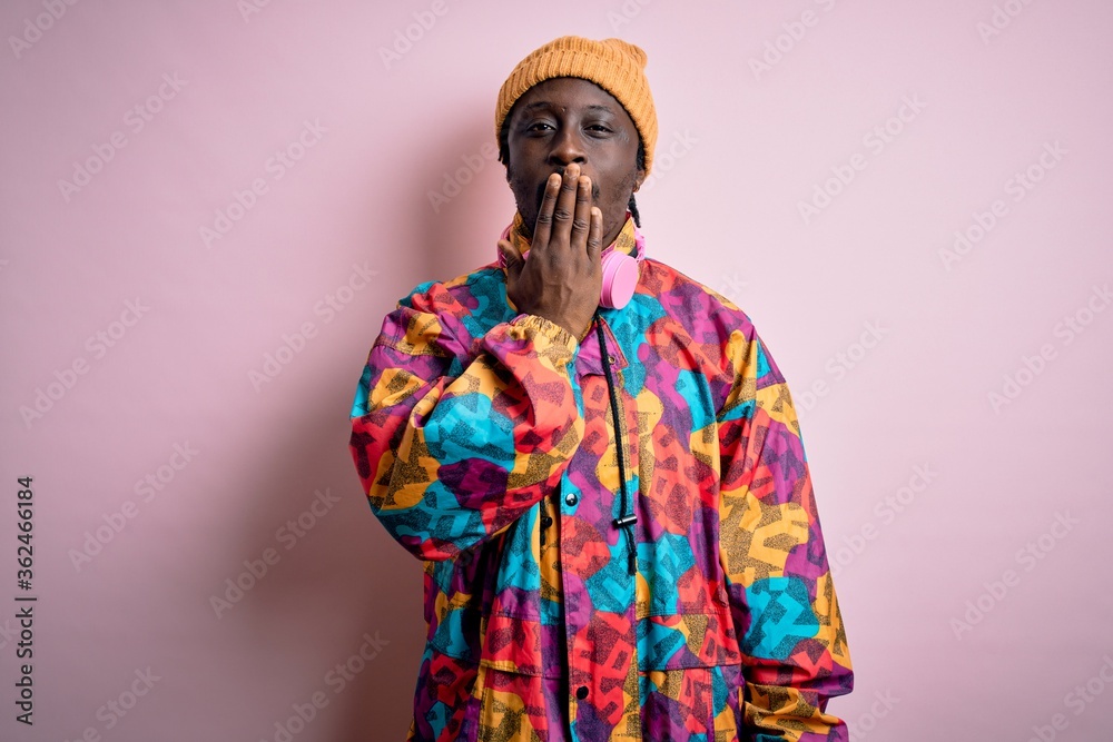 Poster young handsome african american man wearing colorful coat and cap over pink background bored yawning