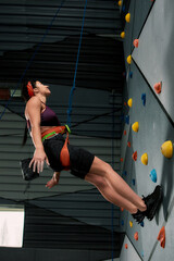 Woman in safety equipment and harness looking up while training on the artificial climbing wall indoors