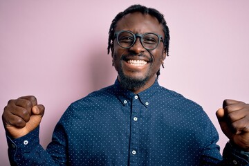 Young handsome african american man wearing casual shirt and glasses over pink background celebrating surprised and amazed for success with arms raised and open eyes. Winner concept.