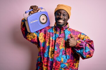 Young african american man listening to music holding portable vintage retro radio happy with big smile doing ok sign, thumb up with fingers, excellent sign