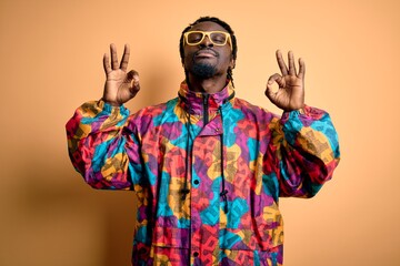 Handsome african american man wearing colorful coat and glasses over yellow background relax and smiling with eyes closed doing meditation gesture with fingers. Yoga concept.