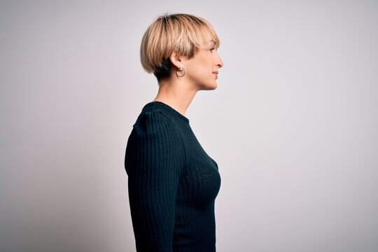Young beautiful blonde woman with modern short hair hairstyle standing over isolated background looking to side, relax profile pose with natural face with confident smile.