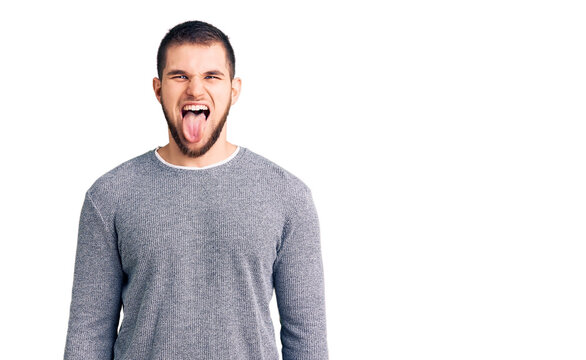 Young handsome man wearing casual sweater sticking tongue out happy with funny expression. emotion concept.