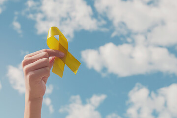 Hands holding yellow gold ribbon over blue sky, Sarcoma Awareness, Bone cancer, childhood cancer...