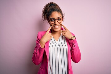 Beautiful african american businesswoman wearing jacket and glasses over pink background Smiling with open mouth, fingers pointing and forcing cheerful smile