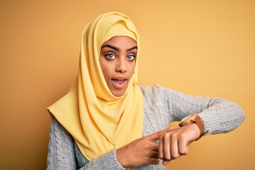 Young beautiful african american girl wearing muslim hijab over isolated yellow background In hurry...