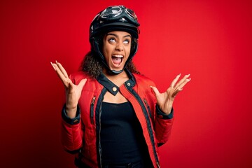 Young african american motorcyclist girl wearing moto helmet and glasses over red background crazy...