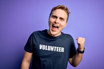 Young handsome redhead man wearing volunteer t-shirt over isolated purple background screaming proud, celebrating victory and success very excited with raised arms