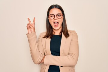 Young beautiful brunette businesswoman wearing jacket and glasses over white background smiling with happy face winking at the camera doing victory sign. Number two.