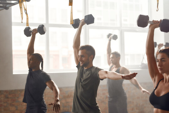One degree of commitment. Group of sportive people lifting dumbbell while having workout at industrial gym. Group training, teamwork concept