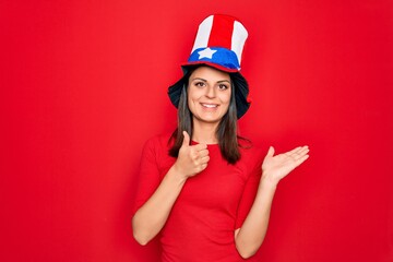 Young beautiful brunette woman wearing united states hat celebrating independence day Showing palm hand and doing ok gesture with thumbs up, smiling happy and cheerful