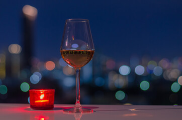A glass of Rose wine with red candle on table and colorful city bokeh light background.