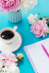 Summer romantic breakfast. Blue vase with peonies, white cup of coffee, notepad for entries with a pen on a blue background.Good morning concept.Copy space, selective focus with shallow depth of field