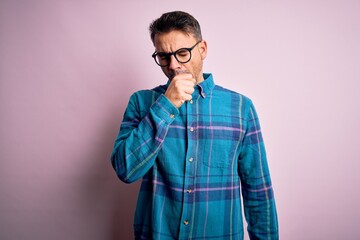 Young handsome man wearing casual shirt and glasses standing over isolated pink background feeling unwell and coughing as symptom for cold or bronchitis. Health care concept.