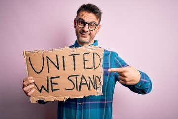 Young handsome activist man asking for union holding banner with united stand message very happy...
