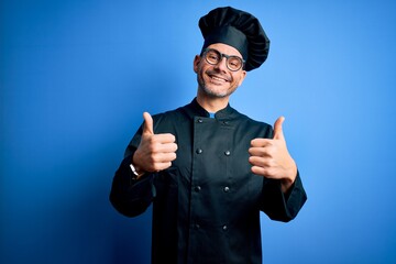 Young handsome chef man wearing cooker uniform and hat over isolated blue background success sign...