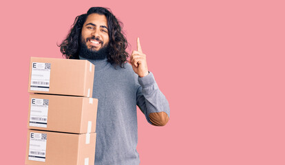 Young arab man holding delivery package surprised with an idea or question pointing finger with happy face, number one