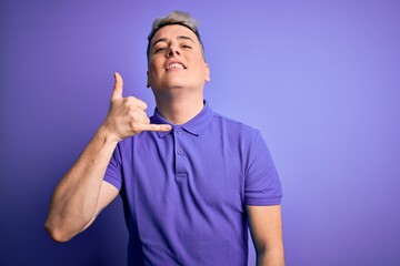 Young handsome modern man wearing casual purple t-shirt over isolated background smiling doing phone gesture with hand and fingers like talking on the telephone. Communicating concepts.