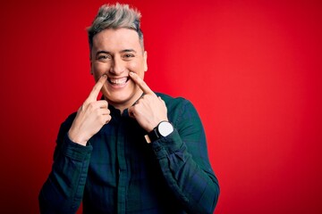 Young handsome modern man wearing elegant green shirt over red isolated background Smiling with open mouth, fingers pointing and forcing cheerful smile