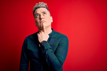 Young handsome modern man wearing elegant green shirt over red isolated background Thinking concentrated about doubt with finger on chin and looking up wondering