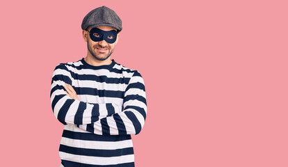 Young handsome man wearing burglar mask happy face smiling with crossed arms looking at the camera. positive person.