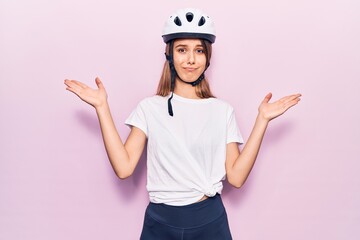 Young beautiful girl wearing bike helmet clueless and confused with open arms, no idea and doubtful face.