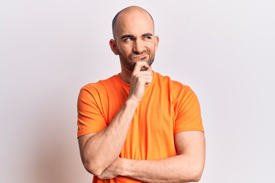Young handsome bald man wearing casual t shirt thinking concentrated about doubt with finger on chin and looking up wondering
