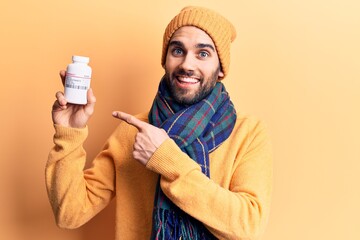 Young handsome man with beard holding bottle of pills smiling happy pointing with hand and finger