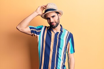 Young handsome man with beard wearing summer hat and shirt confuse and wonder about question. uncertain with doubt, thinking with hand on head. pensive concept.