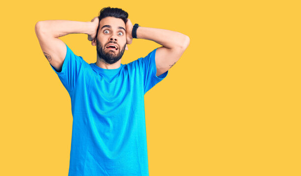 Young handsome man with beard wearing casual t-shirt crazy and scared with hands on head, afraid and surprised of shock with open mouth