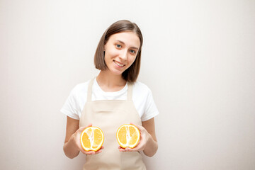 Smiling beautiful girl wearing apron holding two oranges. Woman in apron looking at camera and smiling.