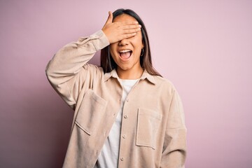 Young beautiful asian woman wearing casual shirt standing over pink background smiling and laughing with hand on face covering eyes for surprise. Blind concept.