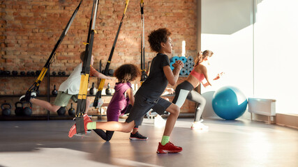 Portrait of teenage kids training using fitness straps in gym with female trainer. Sport, healthy lifestyle, physical education concept