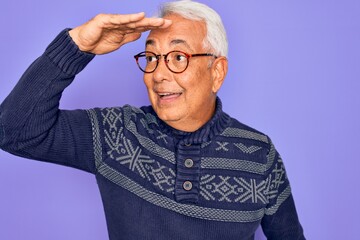 Middle age senior grey-haired man wearing glasses and winter sweater over purple background very happy and smiling looking far away with hand over head. Searching concept.