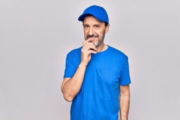 Middle age handsome deliveryman wearing cap standing over isolated white background smiling looking confident at the camera with crossed arms and hand on chin. Thinking positive.