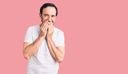 Middle age handsome man wearing casual t-shirt laughing and embarrassed giggle covering mouth with...