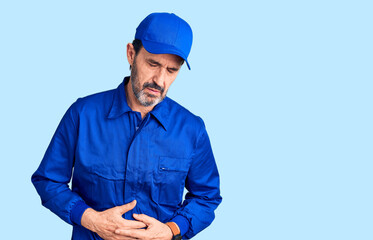 Middle age handsome man wearing mechanic uniform with hand on stomach because indigestion, painful illness feeling unwell. ache concept.