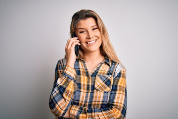 Beautiful blonde woman having conversation talking on the smartphone over white background with a happy face standing and smiling with a confident smile showing teeth