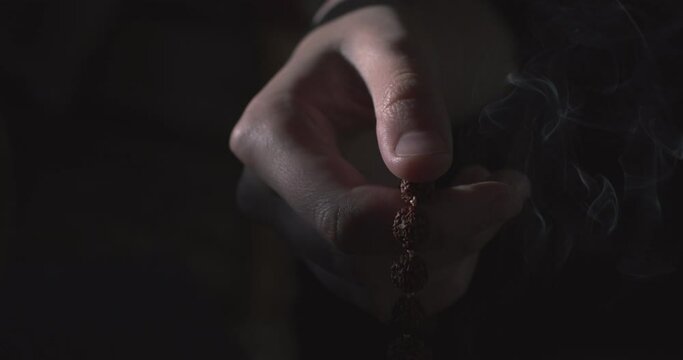 Close up hands holding wooden rosary indoors on black background copy text space. Faceless prayer counting beads slow motion minimalistic shot. Trust hope belief concept. Religious accessories