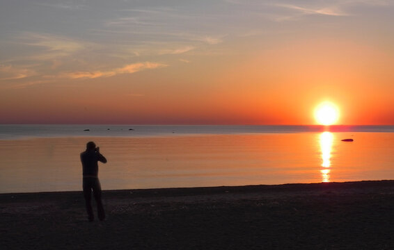 Back view of a silhouette of a man photographing the sun at sunset on the beach on holidays